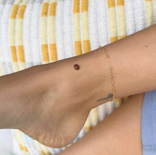 A gold chain anklet against a yellow striped towel
