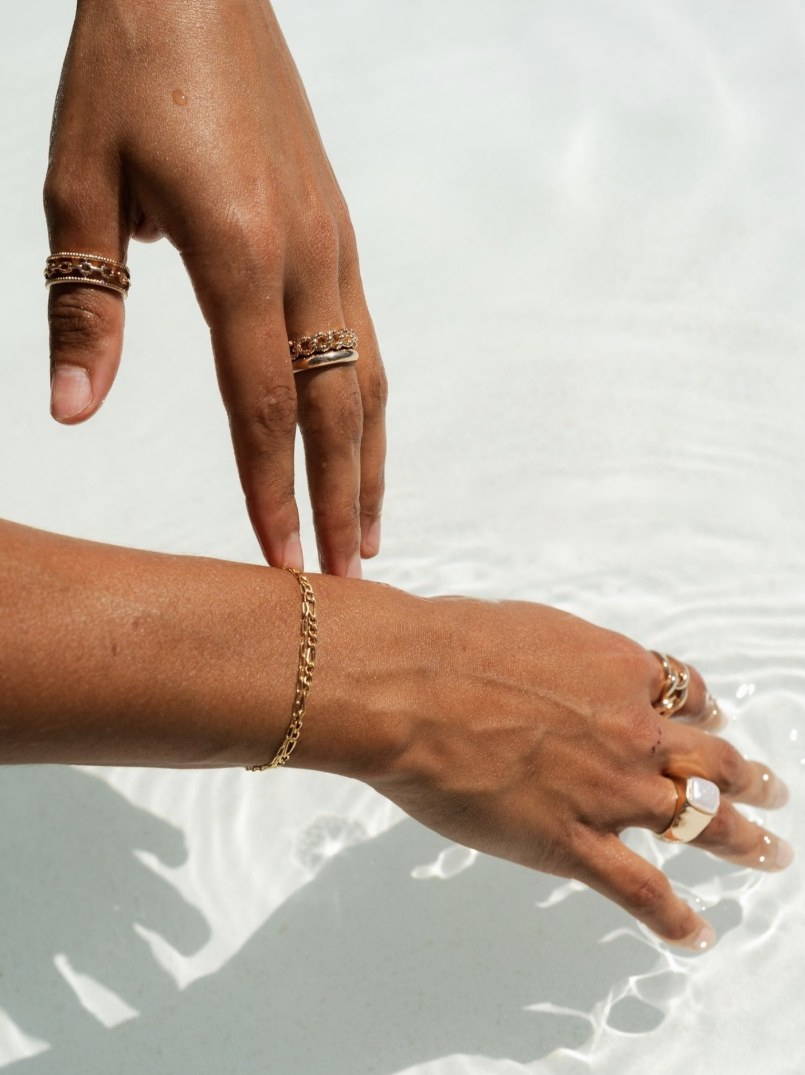 A fine gold chain bracelet on a wrist, hands resting on sunlit water